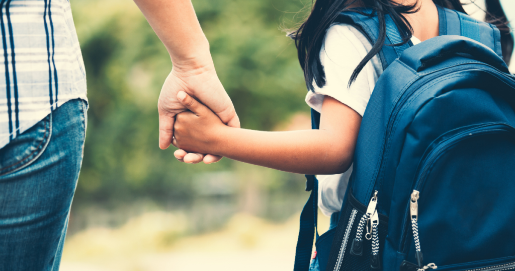 adult holding hands with a child wearing a backpack